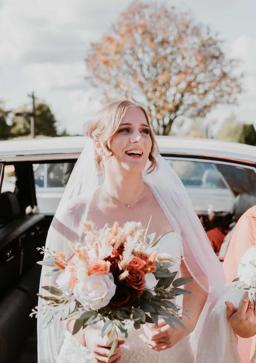 Bride smiling beside her wedding car with her bouquet